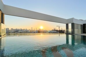 A rooftop swimming pool with a city skyline view at sunset. - Luxe Gardenia 2BR Haven in Dubai (Dubai)