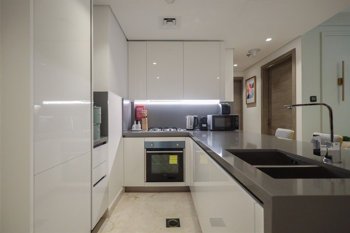 Una cocina moderna con armarios blancos, horno empotrado, microondas y encimera de acero inoxidable.