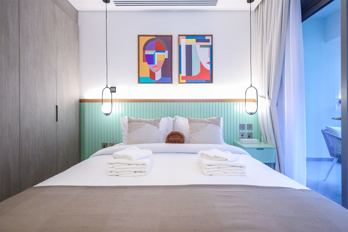 Une chambre d’hôtel avec un lit, deux tableaux au mur, une table de chevet et une vue sur l’extérieur.