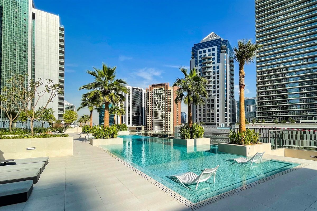 A rooftop pool with lounge chairs, surrounded by palm trees and modern buildings.