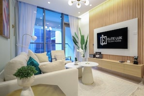 A modern living room with a sofa, a coffee table, a TV, and a large window with curtains. - Elegant 2BR Suite Near Downtown Dubai (Dubai)