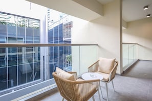 Ein Balkon mit Korbstühlen und einem kleinen Tisch, große Fenster mit Blick auf die Stadt und ein Fliesenboden.