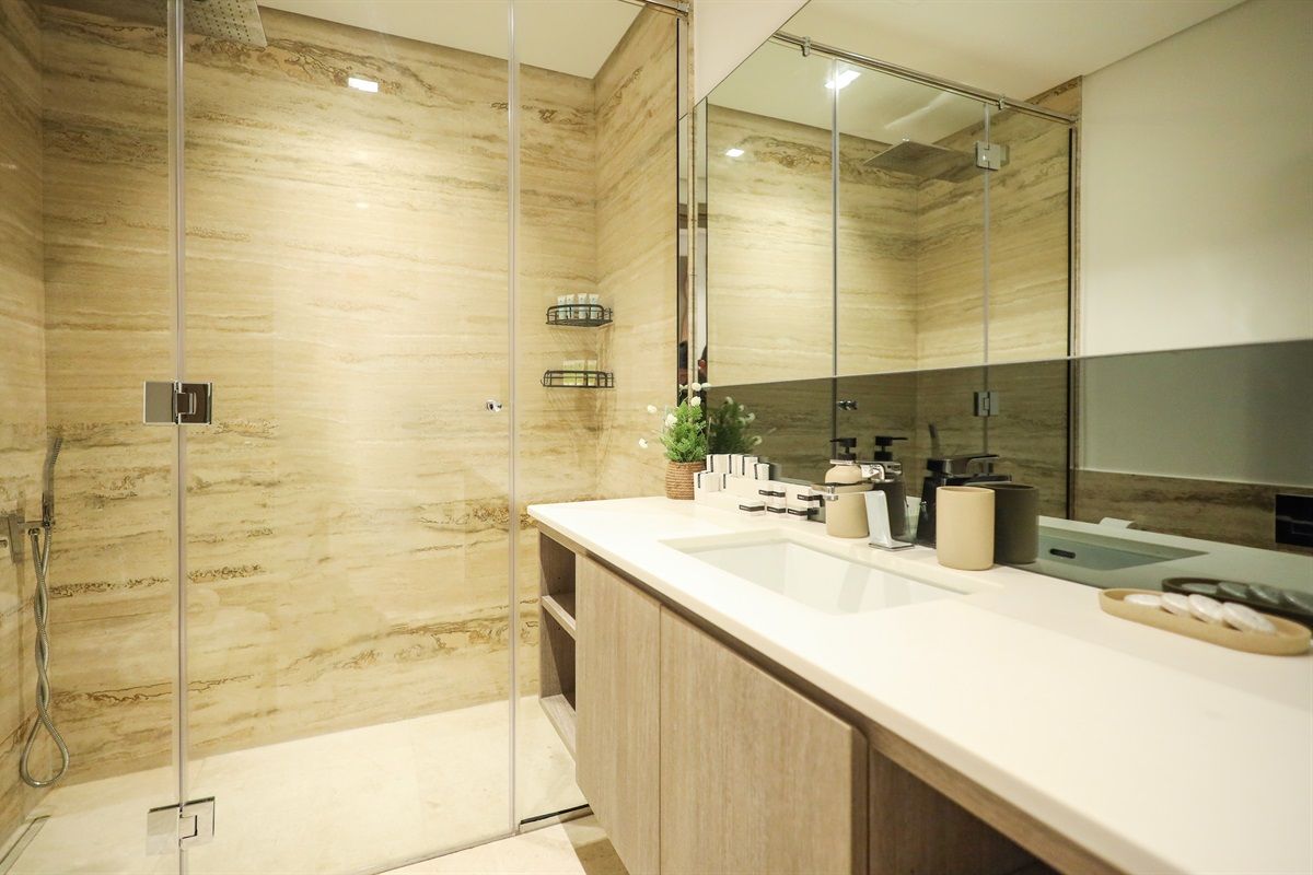 A modern bathroom with a glass-enclosed shower, a large mirror, and a white countertop with toiletries.