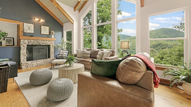 Un salón acogedor con chimenea de piedra, ventanas amplias que ofrecen vistas al bosque y un techo alto con vigas a la vista.