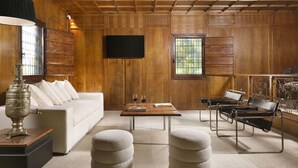A room with a wooden paneled wall, a white sofa, a wooden coffee table, two white poufs, a TV mounted on the wall, and a window with a view. - Beautiful private villa for 4 guests with A/C, WIFI, private pool and TV (La Giustiniana)