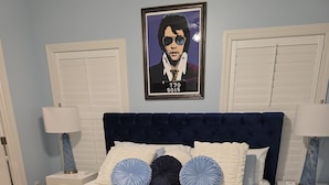 A bedroom with a large bed, two nightstands, a framed picture on the wall, and a window with blinds. - The Sugar Shack Cottage with Hot Tub (Tupelo)