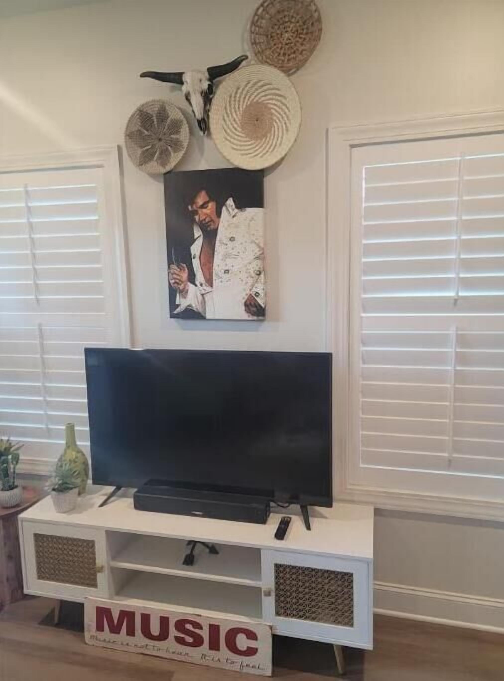 Un salon avec un téléviseur à écran plat posé sur un meuble blanc, un tableau encadré au-dessus du téléviseur et une enseigne « MUSIQUE » sous le meuble.