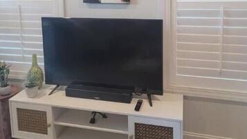 Un salon avec un téléviseur à écran plat posé sur un meuble blanc, un tableau encadré au-dessus du téléviseur et une enseigne « MUSIQUE » sous le meuble.