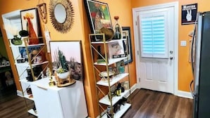 A room with wooden flooring, a white table, and a white door. There are shelves with various items and a mirror on the wall. - The Sugar Shack Cottage with Hot Tub (Tupelo)