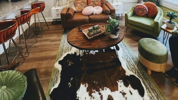 A living room with a brown leather sofa, a green armchair, a wooden coffee table, and a cowhide rug. - The Sugar Shack Cottage with Hot Tub (Tupelo)