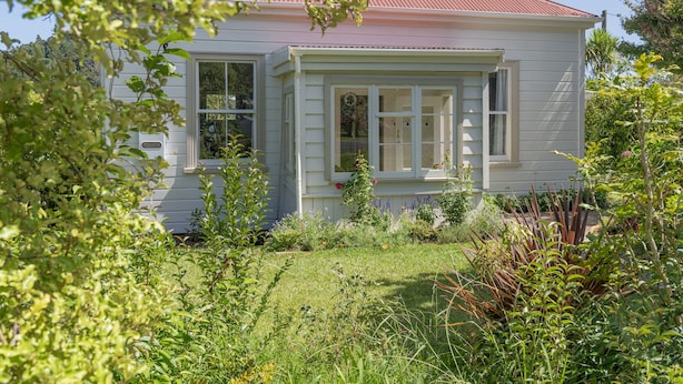 Une maison blanche avec un toit rouge, entourée d’une végétation luxuriante et d’un jardin bien entretenu.