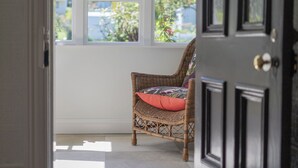 Une chaise en osier avec un coussin rouge, dans une pièce dotée d’une grande fenêtre.