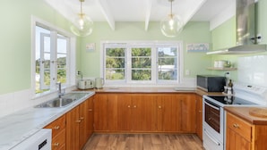 Une cuisine avec des meubles en bois, un évier en acier inoxydable, une cuisinière blanche et une grande fenêtre donnant sur un paysage verdoyant.