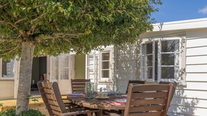 Une terrasse extérieure en bois, avec une table dressée pour le repas, entourée de chaises en bois, sous un arbre.