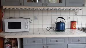Una cocina con armarios grises, un microondas blanco, una tetera y un bote de café.