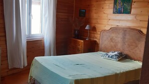 Una habitación con paneles de madera, una cama, una mesita de noche, una lámpara y una ventana con cortinas.