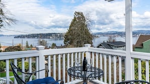 A balcony with a table and chairs overlooking a lake and distant town. - Lake Washington View Home with Hot Tub BBQ Garden (Seattle)