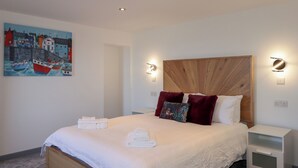Una cama bien hecha con sábanas y toallas blancas, un cabecero de madera y un cuadro con barcos en la pared.