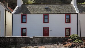 Un edificio blanco con marcos y puerta rojos, situado en una zona montañosa y rocosa.