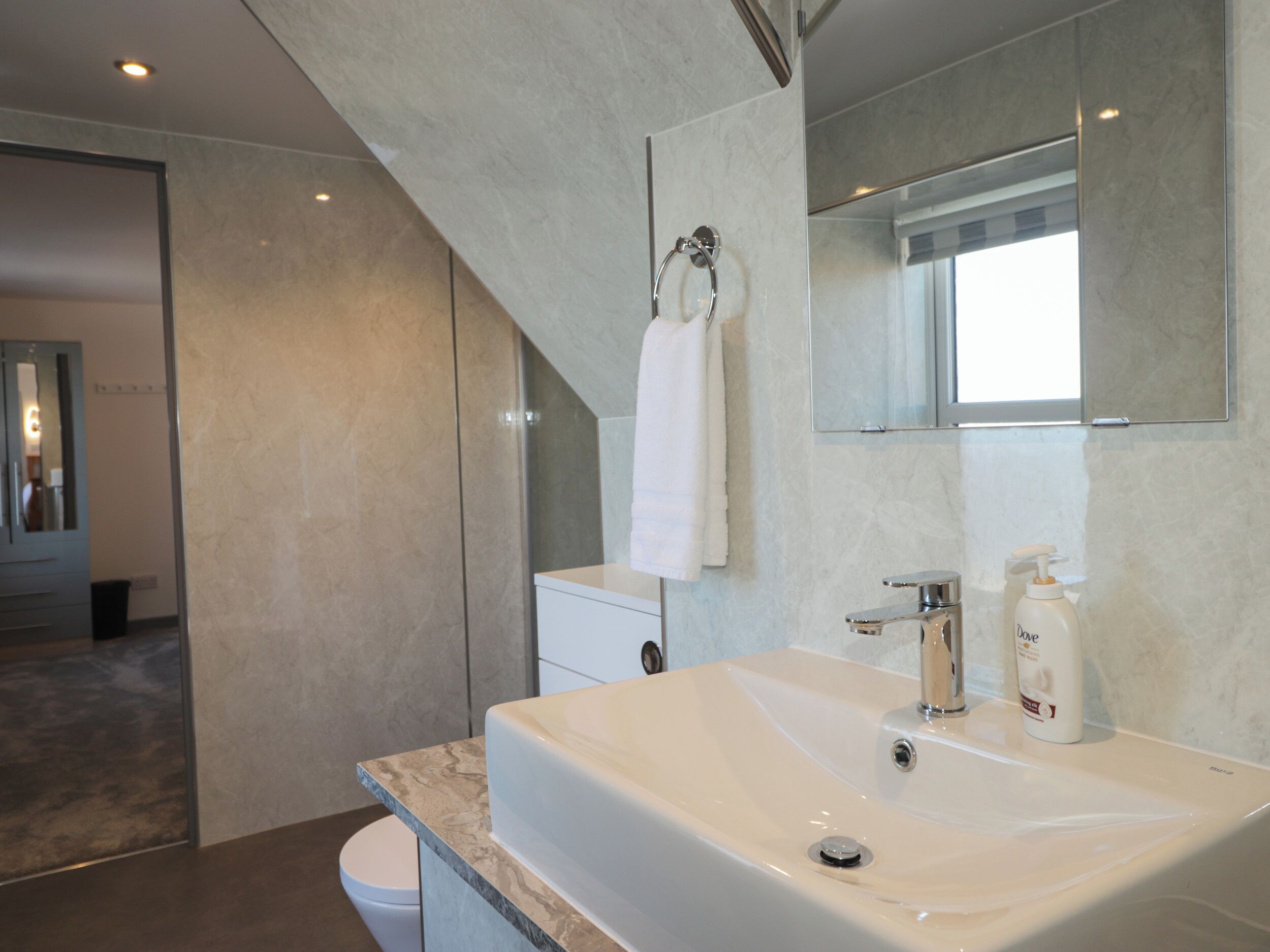 Un baño moderno con un lavamanos grande, un espejo y una toalla colgada en un perchero.