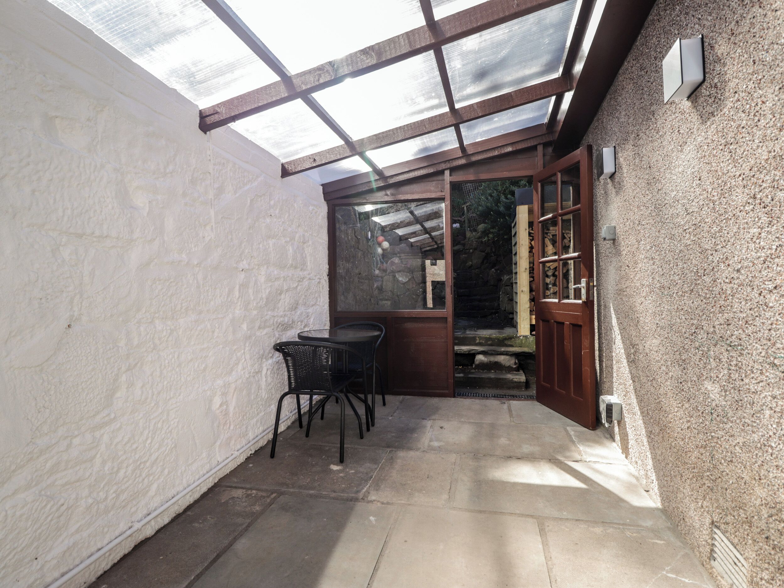 A covered patio area with a table and chairs, a wooden door, and a stone wall.