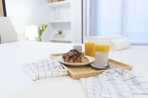 A breakfast tray with a pastry, a cup of coffee, and a glass of orange juice on a bed.