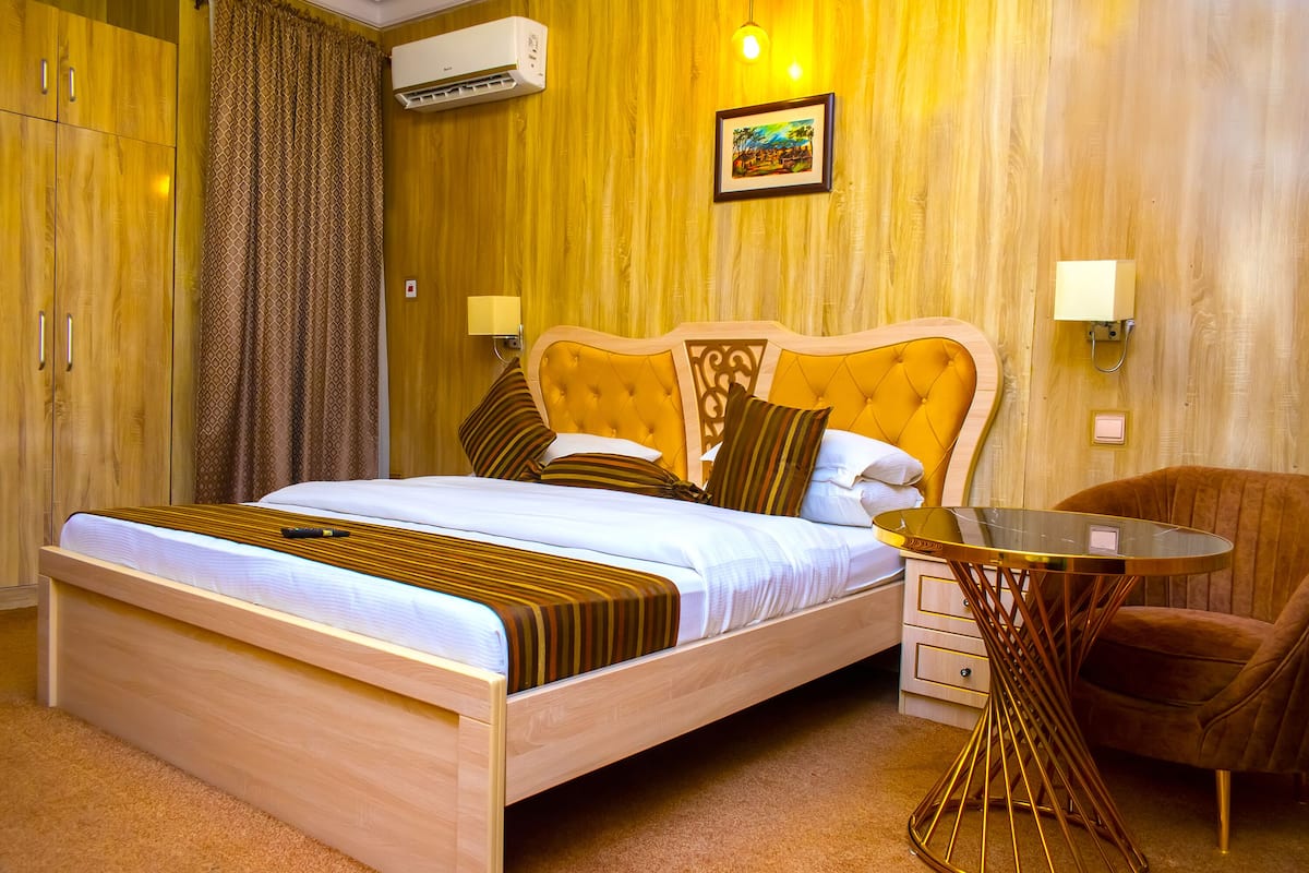 A hotel room with a wooden bed, a glass table, a brown chair, and a picture on the wall.