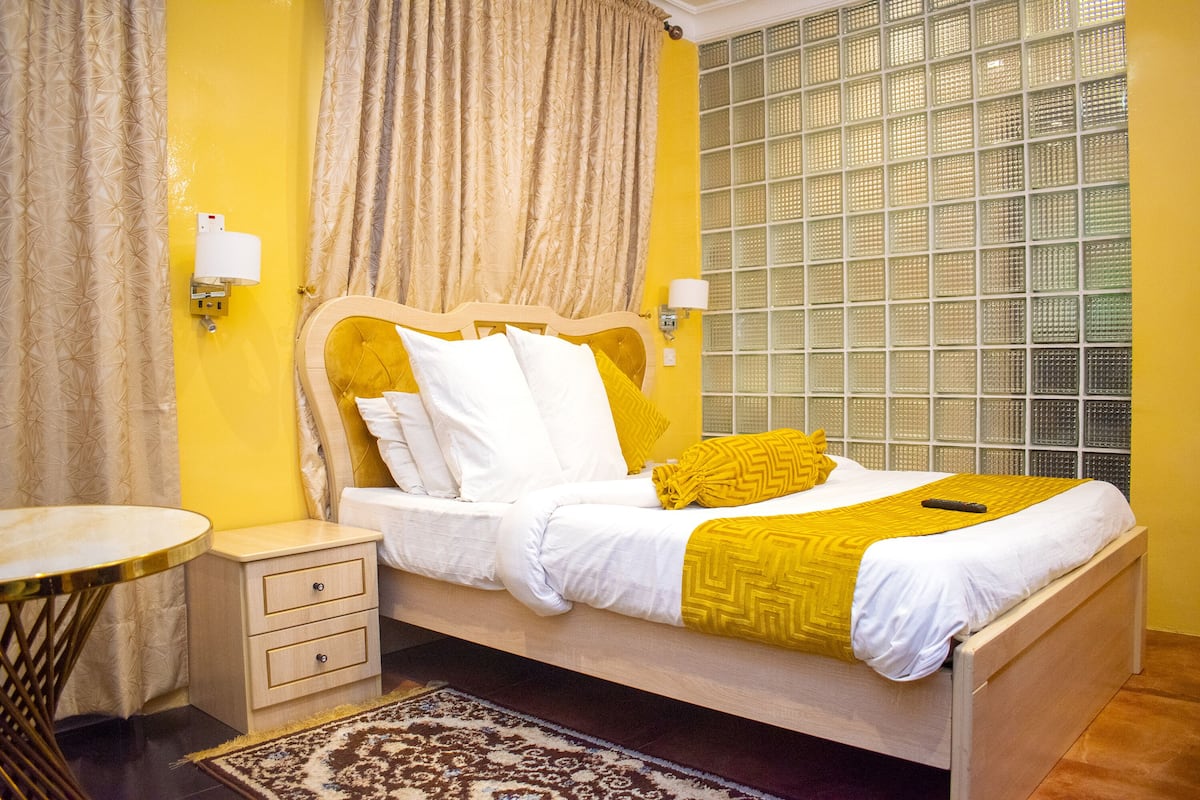 A bedroom with a bed, bedside tables, a nightstand, a patterned rug, and a window with a view.