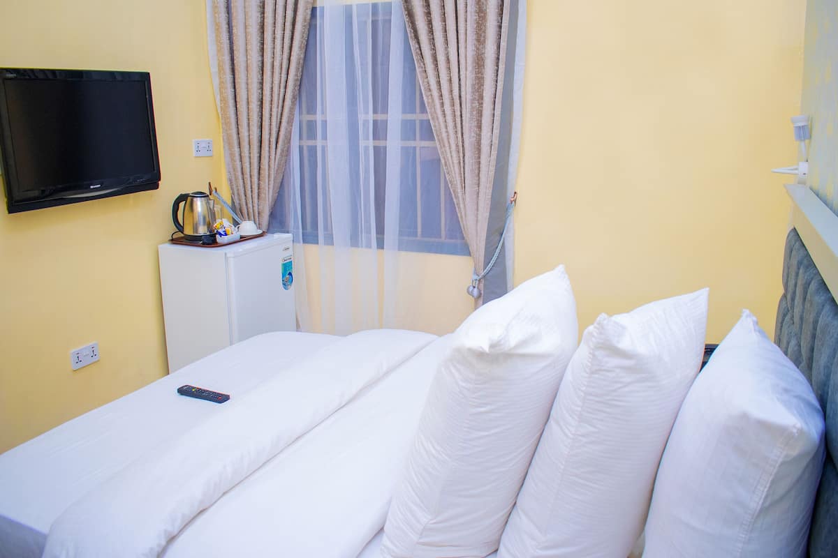 A hotel room with a bed, a television mounted on the wall, a small refrigerator, and a window with curtains.