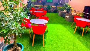 Un patio con césped artificial verde, sillas rojas y una planta en maceta.