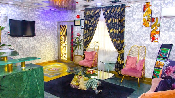 Una sala de estar moderna con una mesa de centro de vidrio, dos sillones rosados, un televisor y una planta decorativa.