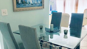 Un comedor con una mesa de vidrio, cuatro sillas y un cuadro en la pared.