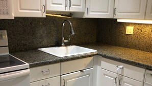 Una cocina con gabinetes blancos, encimera de granito, pileta de acero inoxidable y horno empotrado.