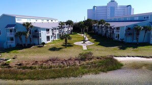 A beachfront hotel with multiple-story buildings, a central pathway, and palm trees. - Chateau by the Bay, Close to Restaurants and Bars, Walk to the Gulf or Bay- W209 (Pensacola Beach)