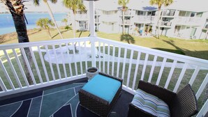 A balcony with wicker furniture, a small table, and a view of a building and palm trees. - Chateau by the Bay, Close to Restaurants and Bars, Walk to the Gulf or Bay- W209 (Pensacola Beach)