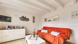 Un salon avec une table basse blanche, un canapé orange et un téléviseur à écran plat fixé au mur.