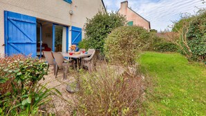 Une maison avec un jardin, une table avec des chaises et une porte bleue.