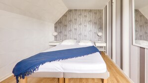 Une chambre à coucher avec un grand lit, un plaid bleu, du linge de lit blanc et une table de chevet avec une lampe.