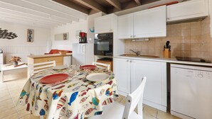 Une cuisine avec des meubles blancs, un lave-vaisselle Bosch et un coin repas avec une table mise pour deux personnes.