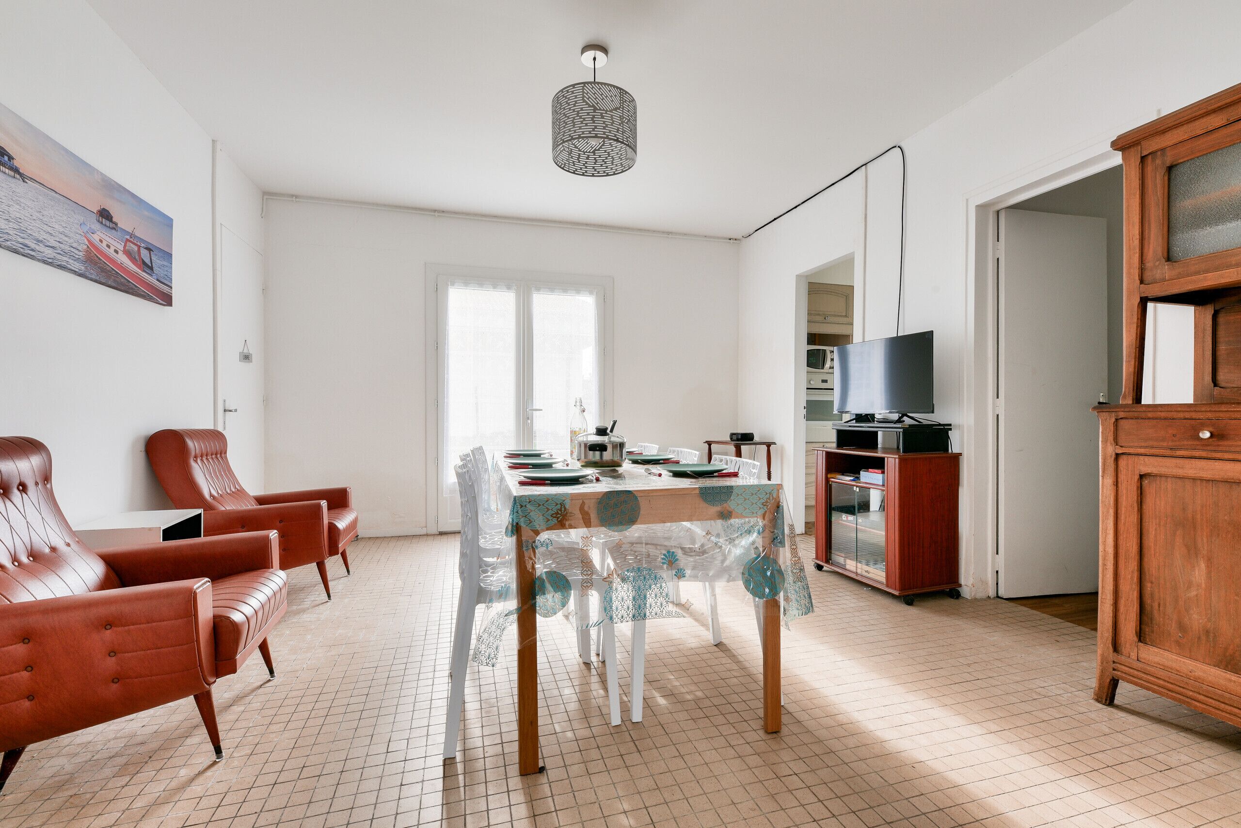 Un coin repas avec une table dressée pour quatre personnes, entouré de fauteuils en cuir, d’un meuble en bois et d’un téléviseur.