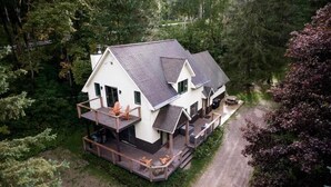 Une maison à deux étages dotée d’un balcon et d’une terrasse, entourée d’une forêt dense.