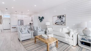 A modern living room with a white sofa, a wooden coffee table, and a grey armchair. - She Sells Seashells TC 8203 (Port Aransas)