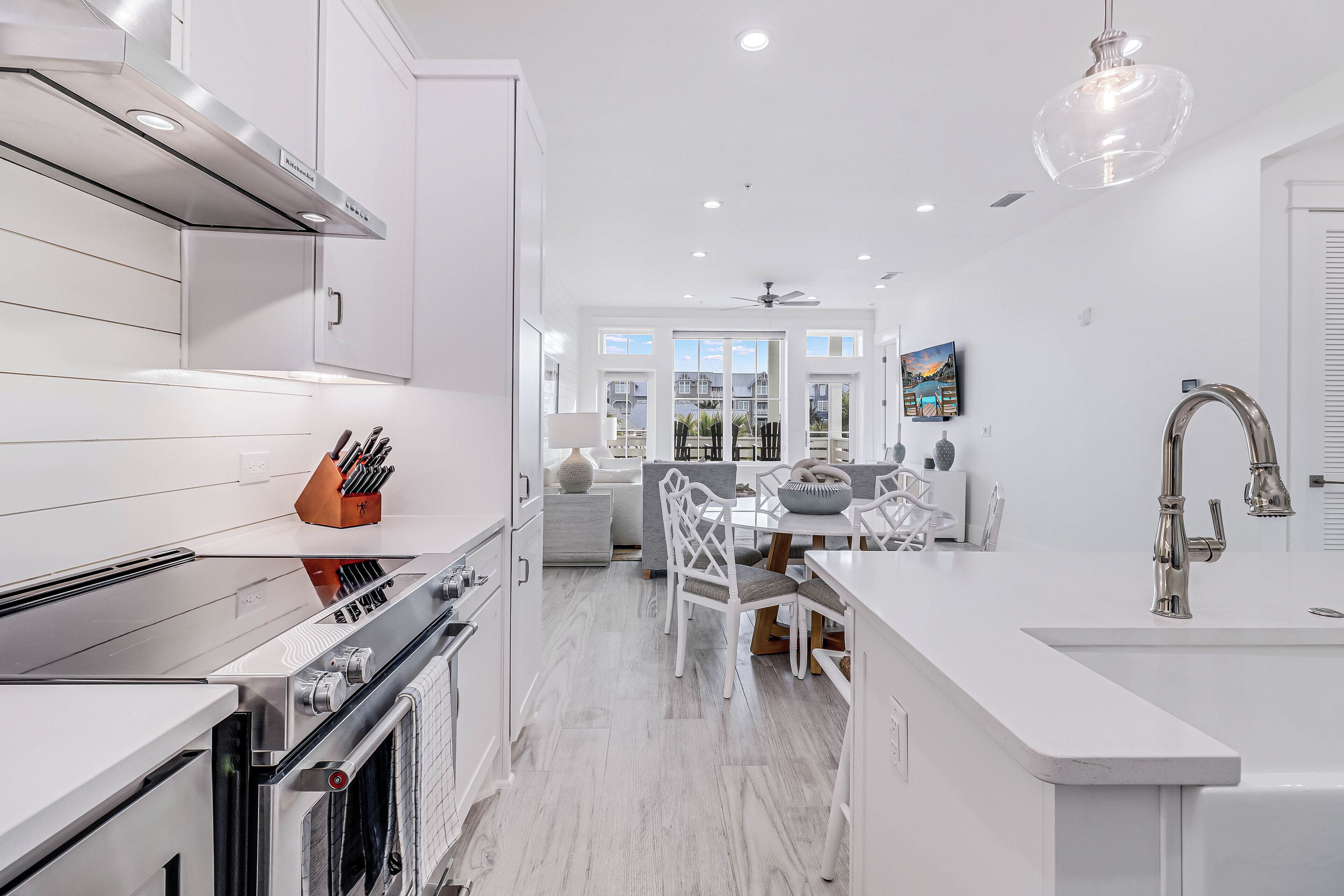 A modern kitchen with white cabinetry, a built-in oven, and a dining area with white chairs and a table.