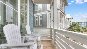 A wooden deck with white Adirondack chairs, a white railing, and a view of a gray building with multiple windows. - Easy Like Sunday Morning TC 8204 (Port Aransas)