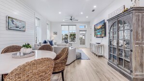 A spacious living room with a dining area, featuring a large wooden cabinet with glass doors, a ceiling fan, and a view of the outdoors through large windows. - Easy Like Sunday Morning TC 8204 (Port Aransas)