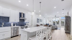 A modern kitchen with white cabinetry, a large island with bar stools, and a blue-tiled backsplash. - Easy Like Sunday Morning TC 8204 (Port Aransas)