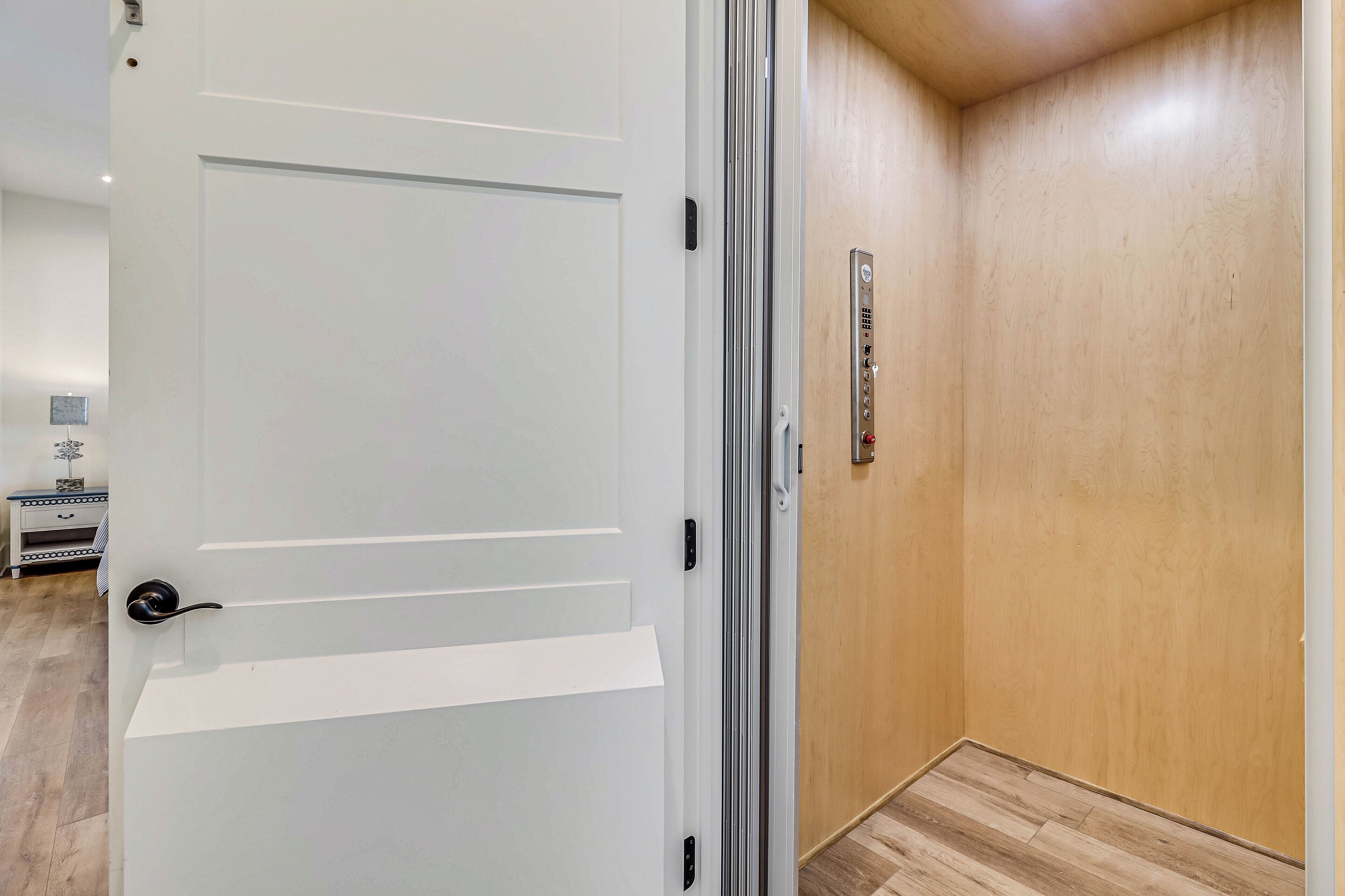 Hotellihuone, jossa on valkoinen ovi, puinen seinä ja seinään asennettu termostaatti.