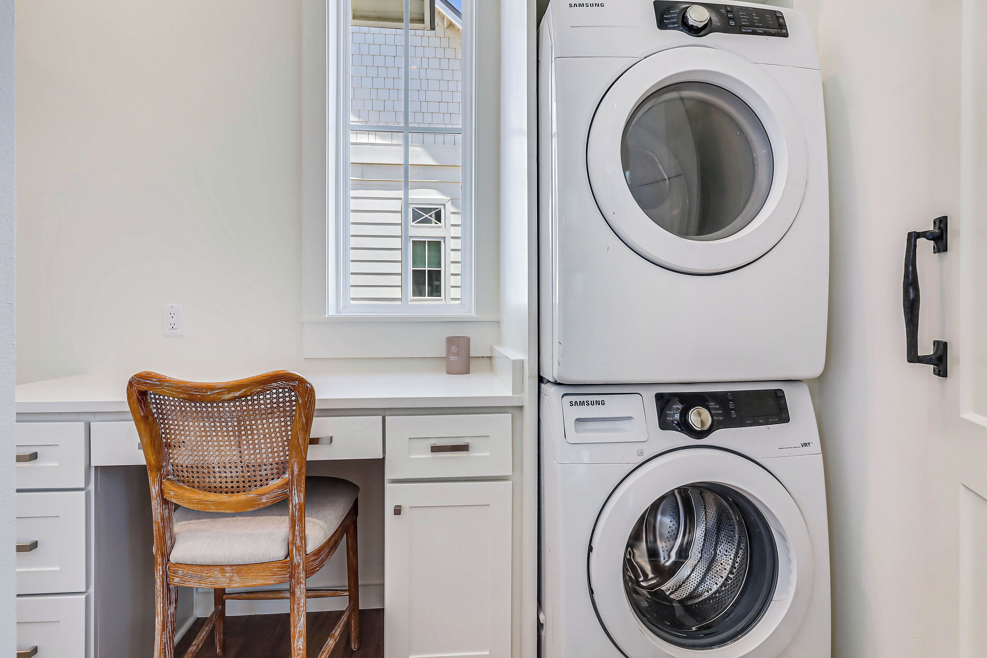 A laundry area with a washing machine, a chair, and a window with a view of a building.