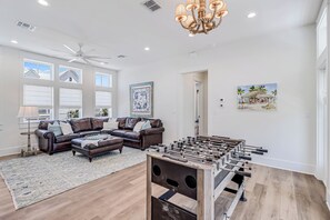 A spacious living room with a foosball table, leather sofas, a chandelier, and large windows. - Shell Yeah! 320 COA (Port Aransas)