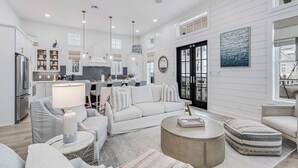 A spacious living room with a large sofa, a coffee table, and a dining area in the background. - Sandy Cheeks 409 COA (Port Aransas)